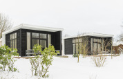 Two modern black river cabins with large windows in snowy surroundings at Holiday Park Mölke in the Netherlands.