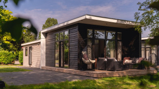 Moderne hytte ved floden med stort terrasseområde og loungemøbler i Holiday Park Mölke, Holland.