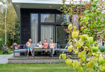 Vier Kinder sitzen auf einem Gartensofa vor einer modernen Lodge im Holiday Park Mölke, Niederlande.