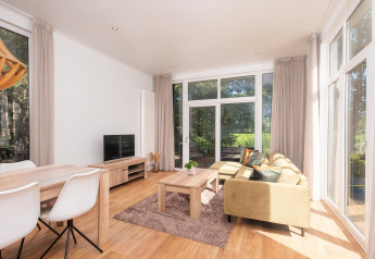 Lichte glampingaccommodatie met gezellige woonkamer, eettafel, bank en grote ramen met uitzicht op de natuur.
