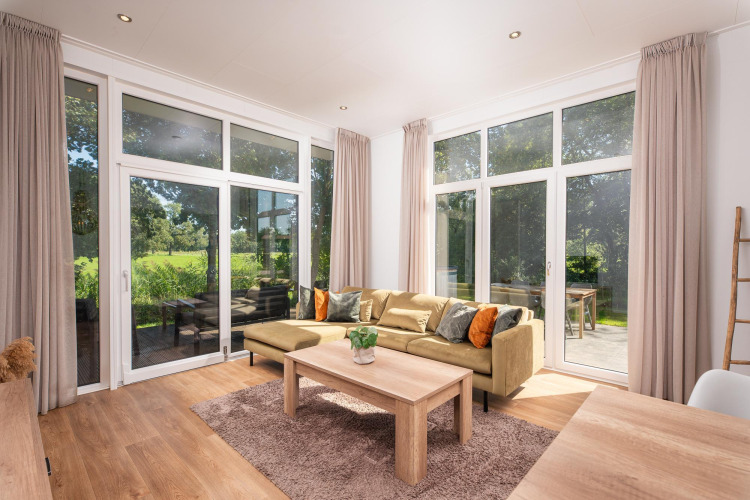 Helles Glamping-Apartment mit großen Fenstern, gemütlichem Sofa, Holztisch und Blick ins Grüne.
