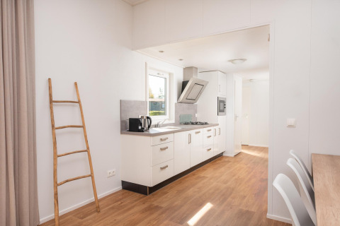 Cocina moderna de glamping con escalera de madera, muebles blancos y luz natural entrando por la ventana.