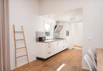 Cocina moderna de glamping con escalera de madera, muebles blancos y luz natural entrando por la ventana.