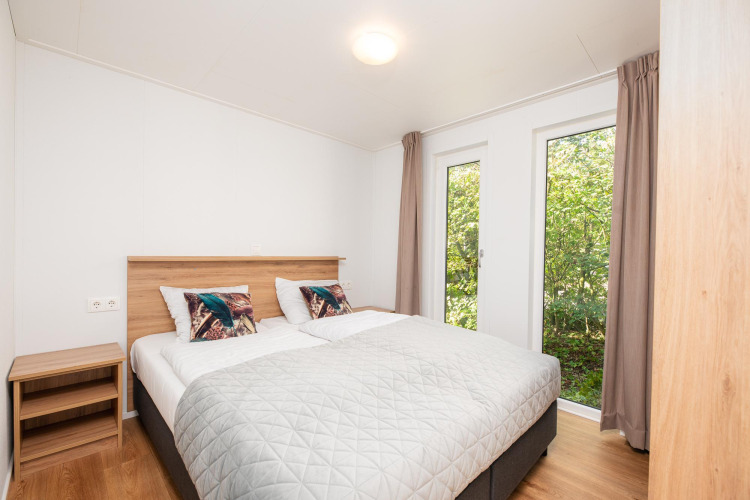 Dormitorio luminoso en alojamiento glamping con cama doble, mesita y grandes ventanales al exterior.