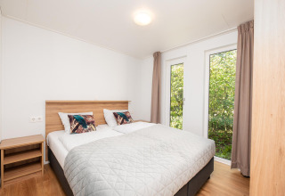 Dormitorio luminoso en alojamiento glamping con cama doble, mesita y grandes ventanales al exterior.