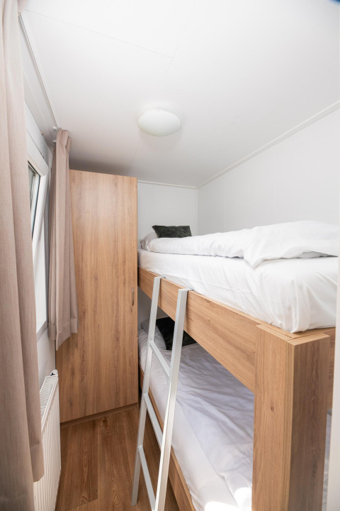 Lichte, smalle kamer met stapelbed, houten kast en raam bij een glamping accommodatie.