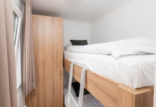 Lichte, smalle kamer met stapelbed, houten kast en raam bij een glamping accommodatie.
