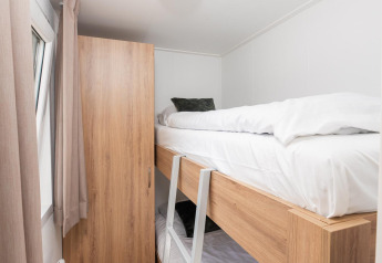 Lichte, smalle kamer met een houten stapelbed, kledingkast en raam in een glamping accommodatie.