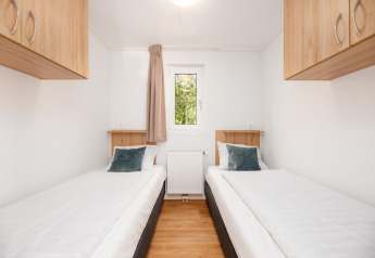 Lichte glampingkamer met twee eenpersoonsbedden, houten kasten, witte muren en een centraal raam.