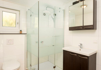 Moderne badeværelse med glasbrusekabine, væghængt toilet og trælook gulv i glampingindkvartering.