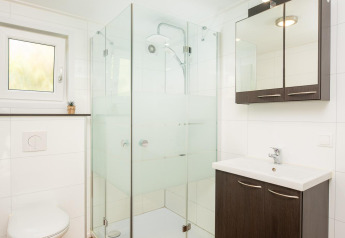Salle de bain moderne avec douche en verre, toilettes suspendues et sol aspect bois en glamping.