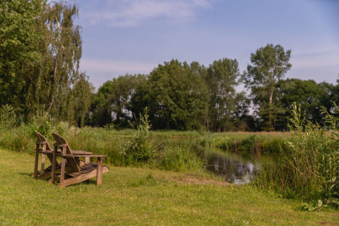 Dos sillas de madera junto a un río rodeado de vegetación en River Cabin, Holiday Park Mölke, Países Bajos.