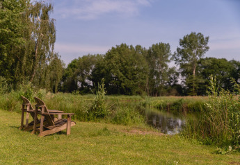 Zwei Holzstühle am Flussufer, umgeben von grüner Natur im Holiday Park Mölke, River Cabin, Niederlande.
