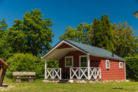 Cabane en bois rouge avec véranda au Scandinavian Lodge, entourée d'arbres verts et d’un ciel bleu.