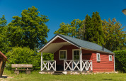Rood houten huisje met veranda bij Scandinavian Lodge, omringd door groene bomen en een blauwe lucht.