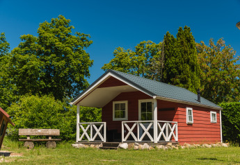 Rood houten huisje met veranda bij Scandinavian Lodge, omringd door groene bomen en een blauwe lucht.