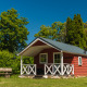 Rød træhytte med veranda ved Scandinavian Lodge, omgivet af grønne træer og klar blå himmel.