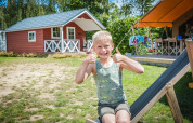 Junge sitzt vor einer skandinavischen Hütte im Holiday Park Mölke in den Niederlanden und zeigt Daumen hoch.