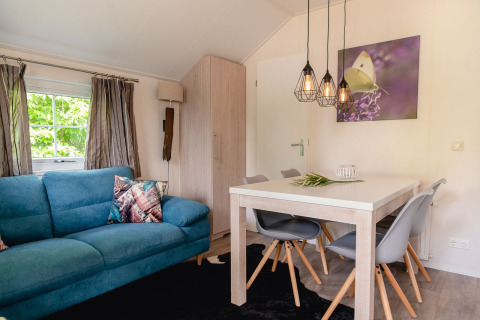 Salon de lodge scandinave avec canapé bleu, table à manger et luminaires modernes à Holiday Park Mölke, Pays-Bas.