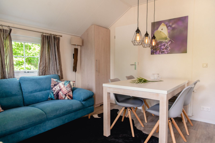 Sala de lodge escandinavo con sofá azul, mesa de comedor y lámparas modernas en Holiday Park Mölke, Países Bajos.