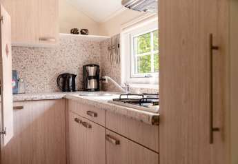 Cocina escandinava luminosa con muebles de madera, cafetera y ventana con vista al jardín verde.