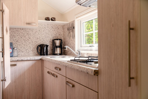 Helles skandinavisches Kücheninterieur mit Holzschränken, Kaffeemaschine und Blick auf den Garten.