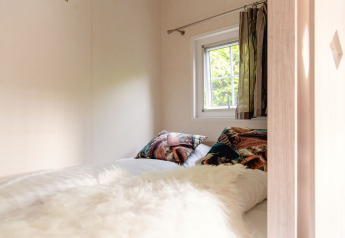 Gemütliches Schlafzimmer mit bunten Kissen und Fensterausblick in einer skandinavischen Lodge in den Niederlanden.