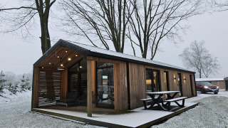 Lodge en bois avec terrasse couverte sous la neige à Wilsumer Berge, Allemagne, entouré d'arbres dénudés.