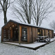 Houten lodge met overdekte veranda en picknicktafel bij Wilsumer Berge, Duitsland, in een besneeuwd landschap.