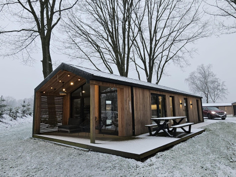 Houten lodge met overdekte veranda en picknicktafel bij Wilsumer Berge, Duitsland, in een besneeuwd landschap.