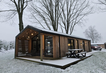 Lodge en bois avec terrasse couverte sous la neige à Wilsumer Berge, Allemagne, entouré d'arbres dénudés.