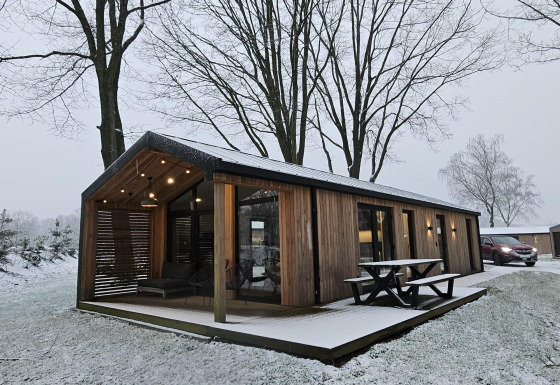 Houten lodge met overdekte veranda en picknicktafel bij Wilsumer Berge, Duitsland, in een besneeuwd landschap.