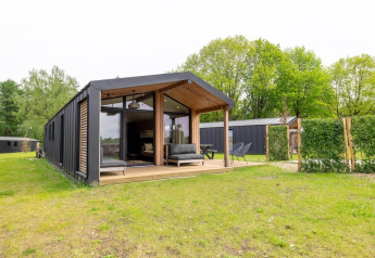 Moderne lodge met grote veranda en glasgevel, omringd door gras en bomen in een groene omgeving.