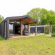 Moderne lodge med stor terrasse og glasfacade, omgivet af grønne træer og græsplæne i naturskønt område.
