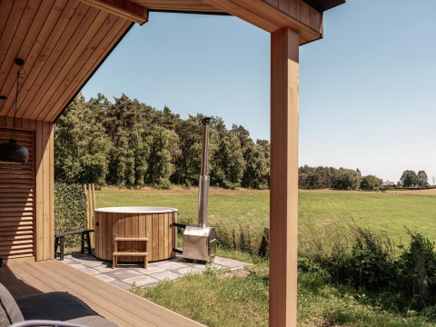 Uitzicht vanaf een houten lodge met buiten hot tub over een groene weide en bos bij Wilsumer Berge, Duitsland.