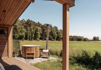 Uitzicht vanaf een houten lodge met buiten hot tub over een groene weide en bos bij Wilsumer Berge, Duitsland.