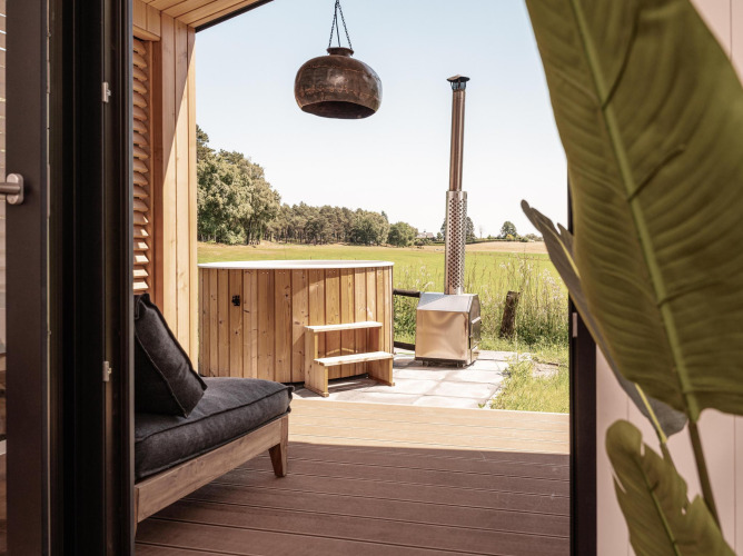 Vista desde una cabaña en Wilsumer Berge, Alemania, con terraza privada, sofá y bañera de hidromasaje exterior.