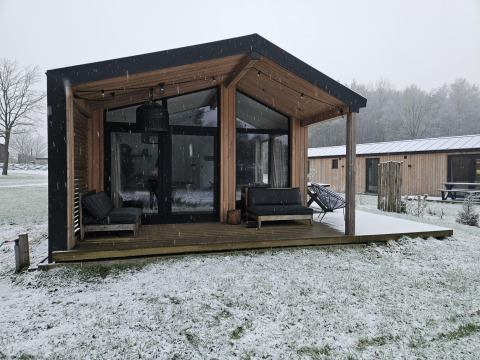 Moderne træhytte ved Wilsumer Berge dækket af sne, set udefra med terrasse og komfortable siddepladser.