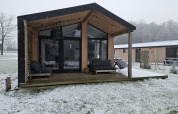 Cabaña moderna de madera en Wilsumer Berge, Alemania, con nieve en el suelo y terraza cubierta.