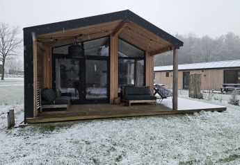 Moderno lodge in legno a Wilsumer Berge, Germania, con nevicata e veranda coperta con poltrone.