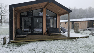 Moderne houten lodge bij Wilsumer Berge, Duitsland, met sneeuw, een overdekt terras en grote ramen.