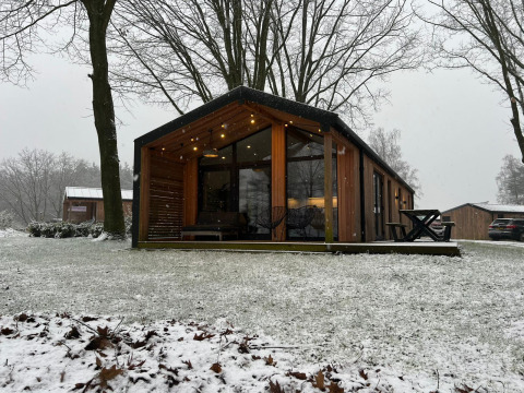 Houten lodge met grote ramen en sfeerverlichting in een witte omgeving bij Wilsumer Berge, Duitsland.