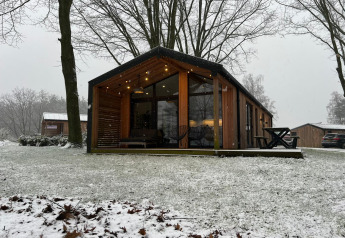 Lodge in legno con grandi finestre e luci esterne in paesaggio innevato a Wilsumer Berge, Germania.