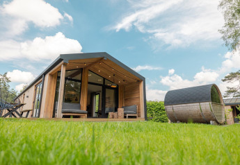 Natur Lodge mit Panorama-Sauna, modernes Holzhaus auf grüner Wiese unter blauem Himmel in Wilsumer Berge, Deutschland.