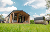 Nature Lodge with panoramic sauna, modern wooden cabin on green grass under blue sky at Wilsumer Berge, Germany.