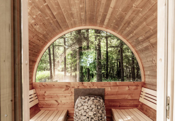 Vista interna di una sauna panoramica in legno con panche e stufa, vista sulla foresta di Wilsumer Berge.