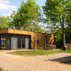 Moderne houten lodge met grote ramen, buitenterras en een hottub omringd door groen en bomen.