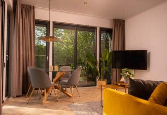 Soggiorno di lodge elegante con ampie finestre, tavolo in vetro, sedie grigie, divano giallo e piante verdi.