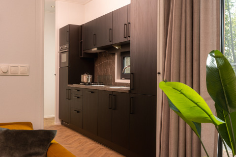 Moderne køkken i en lodge med mørke skabe, gaskomfur, vindue og store gardiner ved siden af stuen.