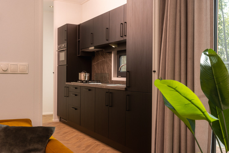 Modern lodge kitchen with dark cabinets, gas stovetop, window, large curtains, and part of living room.